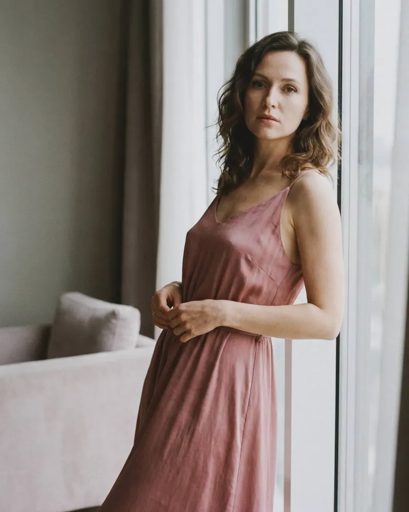 Retrato cercano con vestido de seda rosa junto a ventana grande, fotografía boudoir femenina