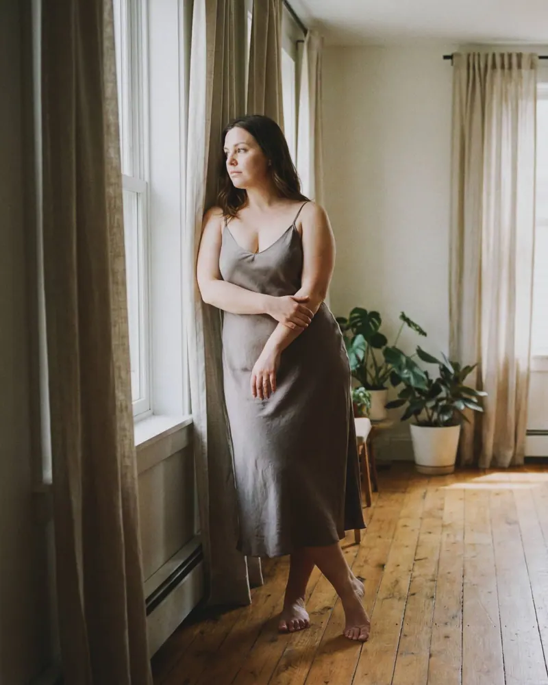 Mujer con vestido de satén gris claro y pies descalzos sobre piso de madera, fotografía boudoir