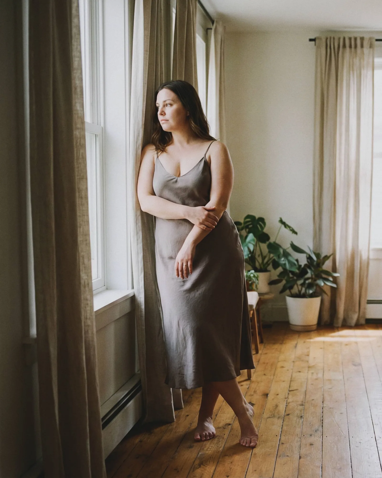 Mujer con vestido de satén gris claro y pies descalzos sobre piso de madera, fotografía boudoir
