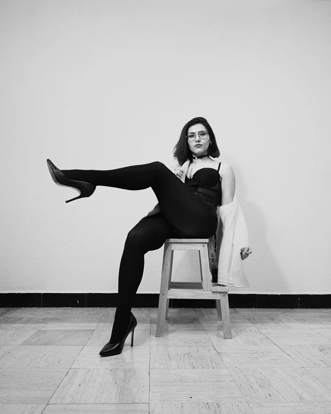 Mujer sobre banco con pierna extendida al frente y lencería negra, boudoir editorial en blanco y negro
