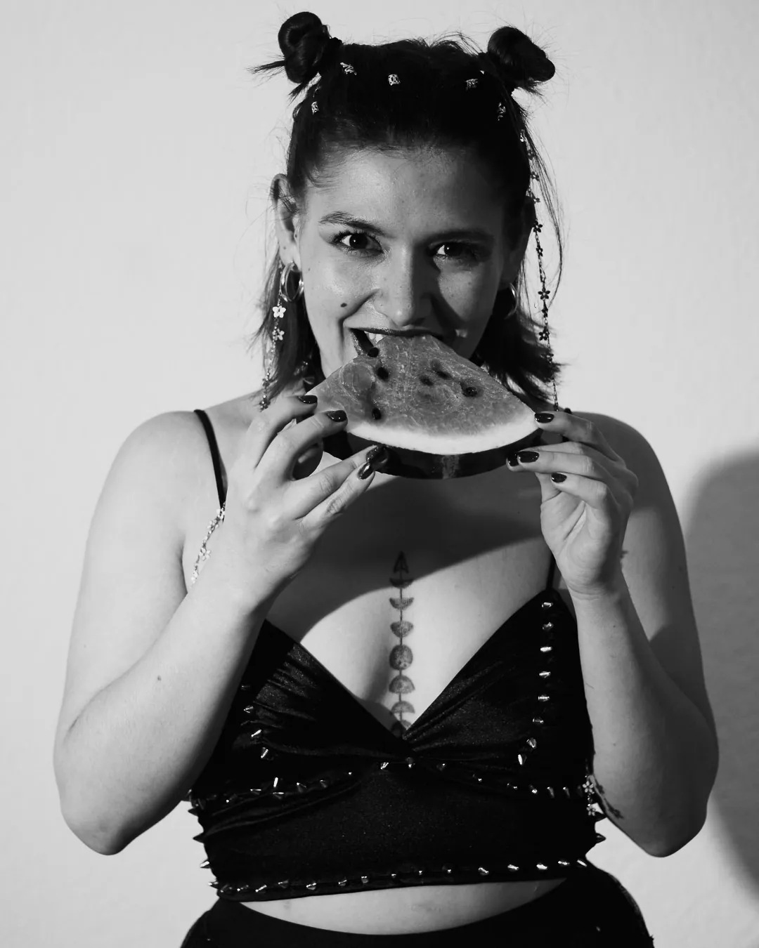 Retrato de mujer mordiendo una rebanada de sandía con top negro de tachuelas, boudoir de estudio en blanco y negro