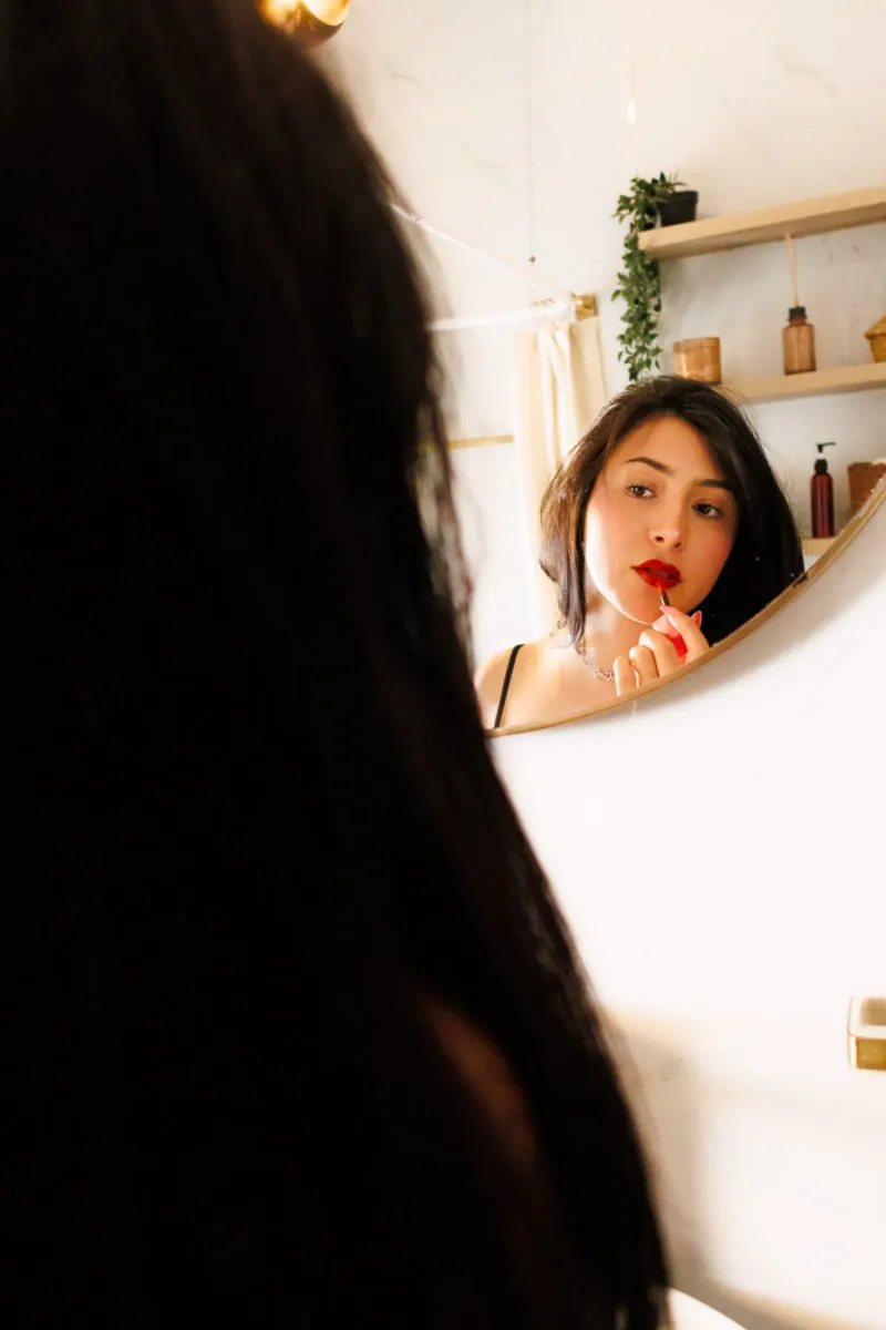 Mujer aplicándose labial rojo frente al espejo, reflejo íntimo sesión boudoir individual CDMX
