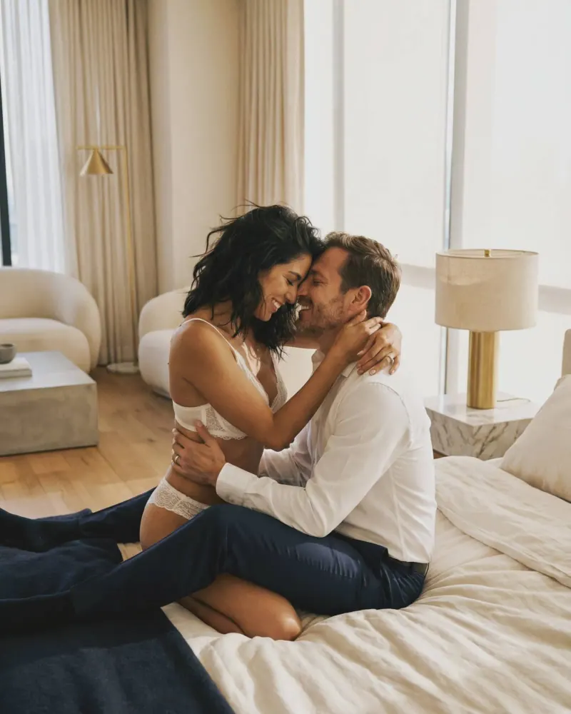 Pareja nupcial boudoir besándose en sillón con velo y lencería, sesión íntima